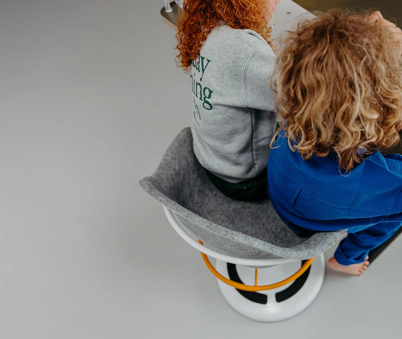 Two children sharing the gray poptop adjustable desk chair