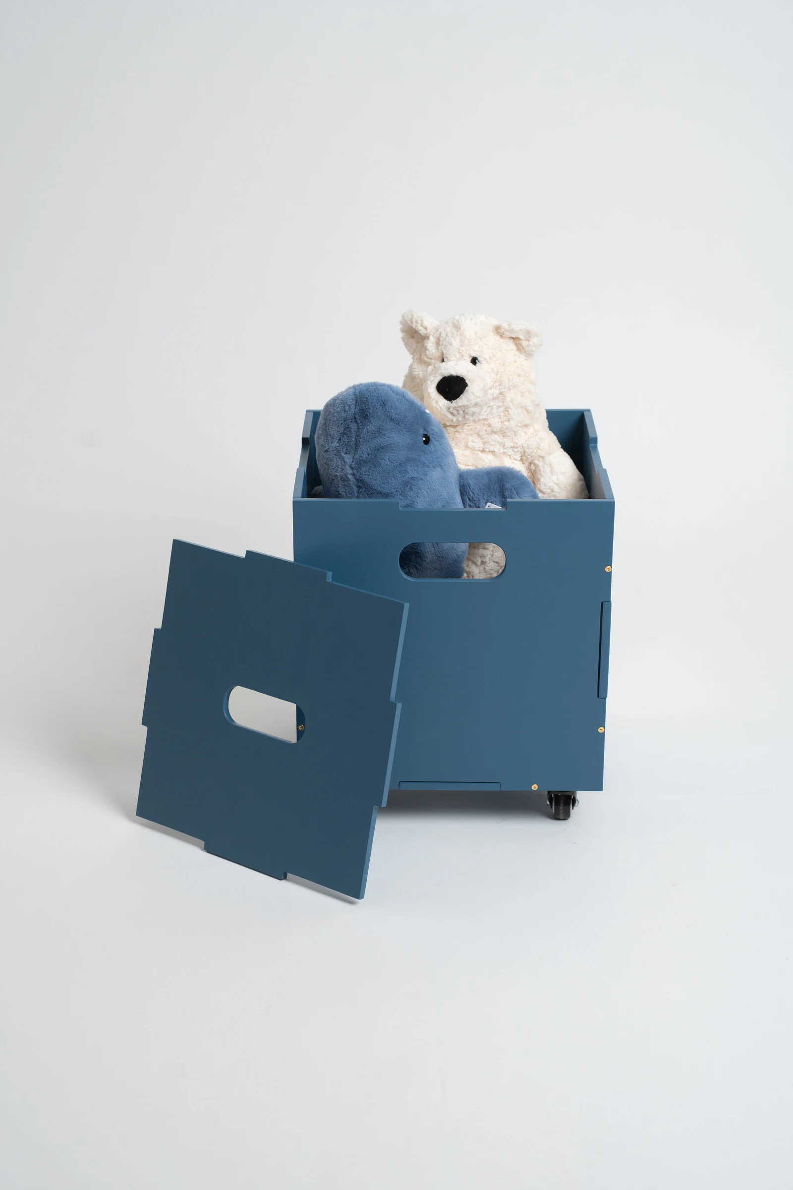 A blue wooden toy box with a hinged lid, shown with a white plush bear and a blue plush toy inside, on a light gray studio background.
