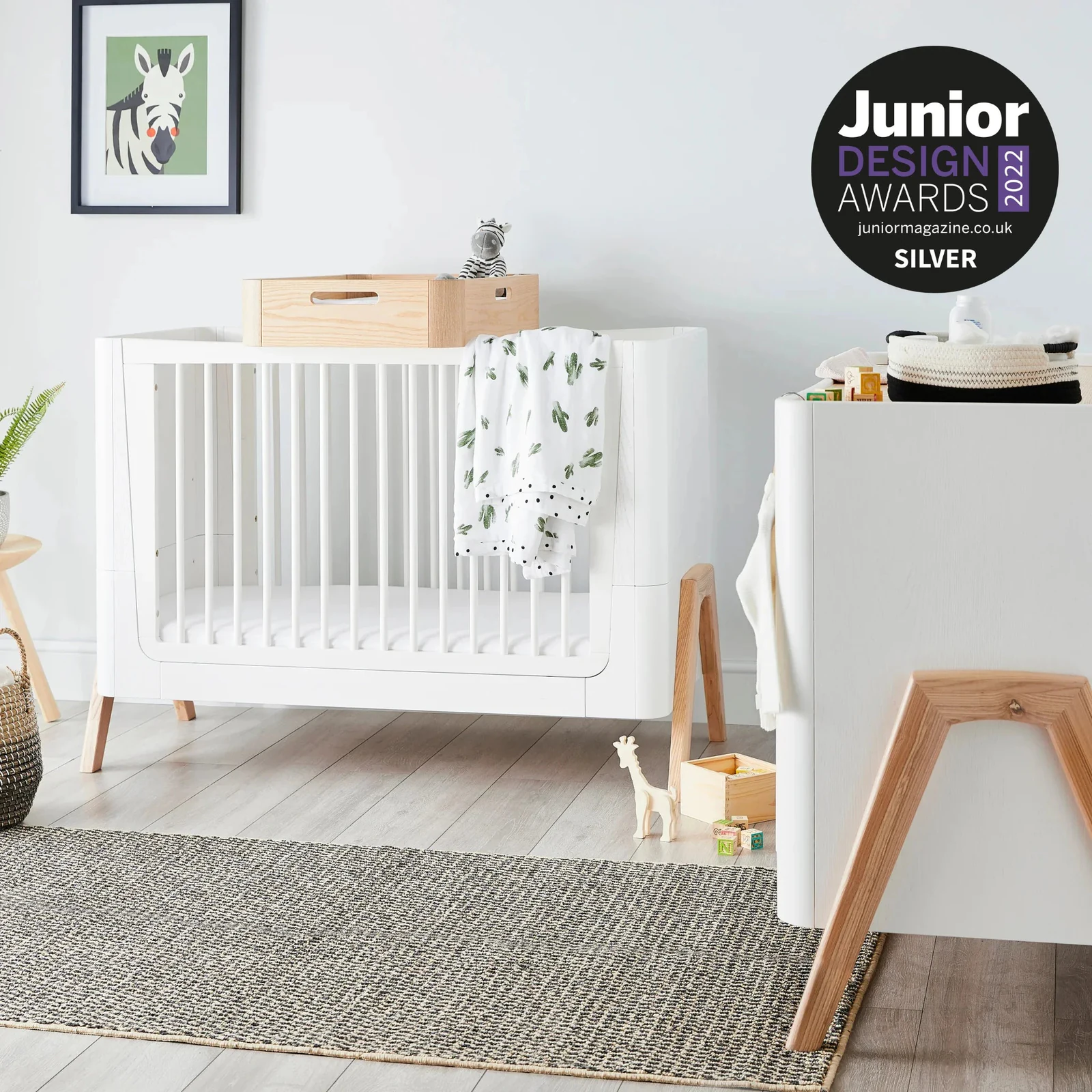 Hera Convertible Cot Bed in a white and natural-wood finish within a styled nursery.