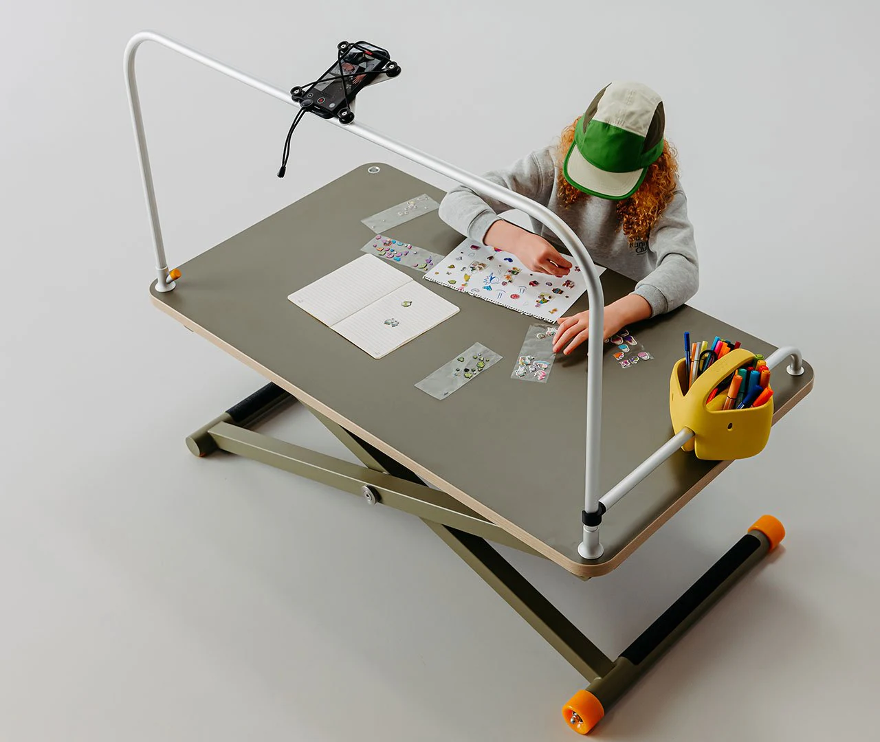 Child working at a green poptop height-adjustable desk with desk lamp
